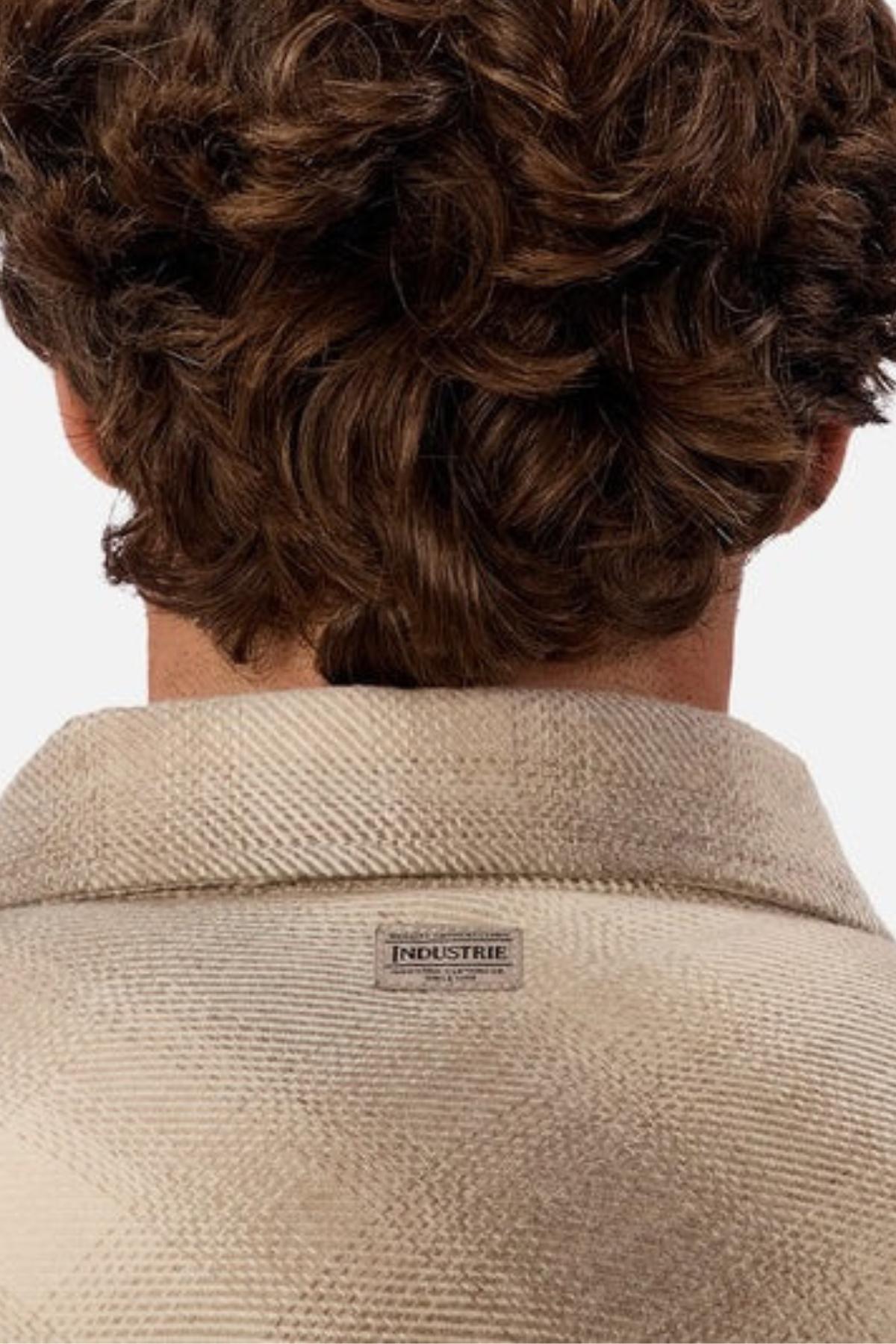 A person with curly brown hair is seen from behind, wearing the Industrie The Highland Jacket in beige—an ideal choice for outdoor adventures.