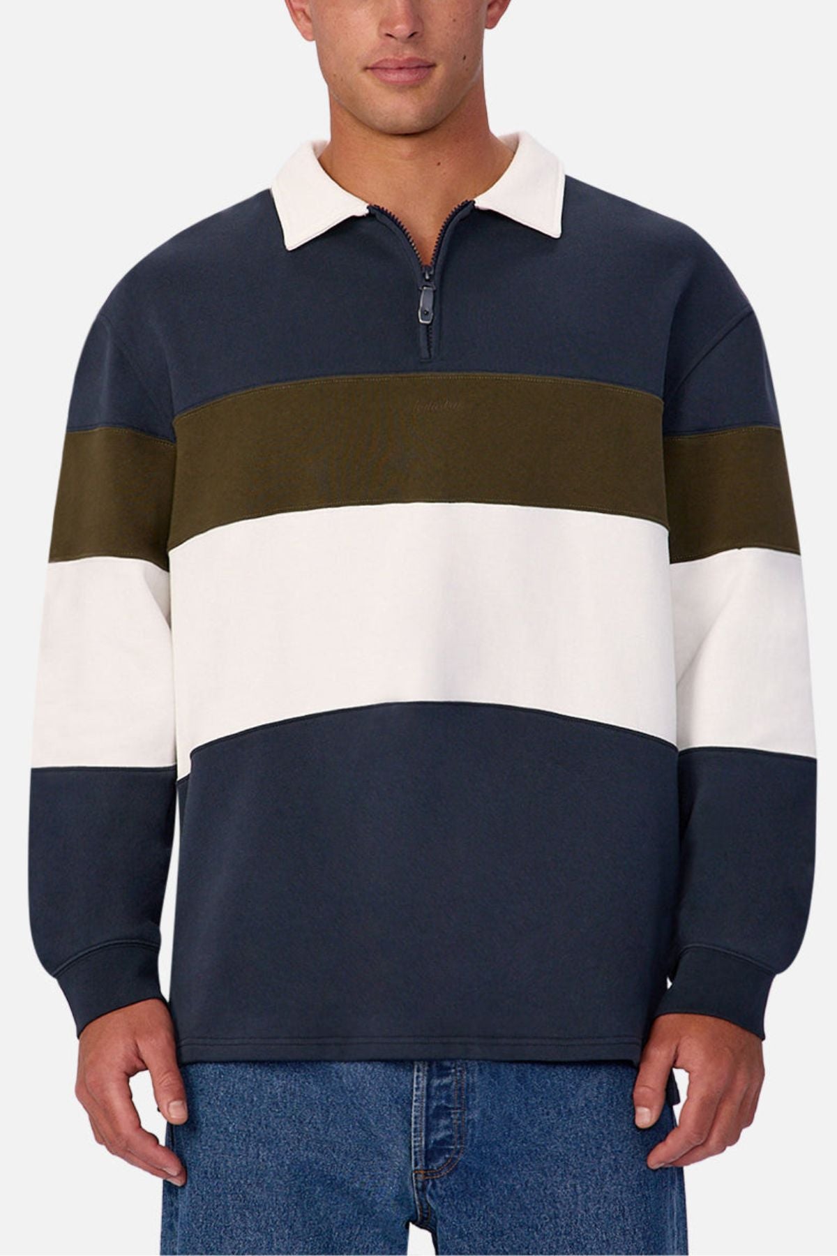 A person wears Industrie The Stanstead Tracktop— a modern long-sleeve pullover with wide navy, olive green, and white stripes and a zip-up collar—paired with blue jeans for a relaxed casual look.