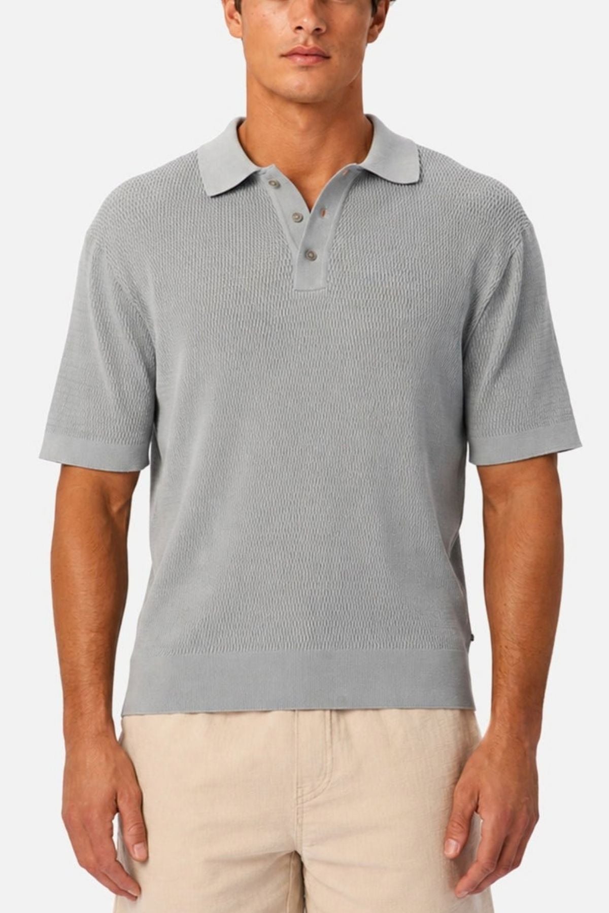 A man wearing the Industrie The Bastien Polo in light gray, featuring short sleeves, a classic collar, and textured fabric, paired with beige pants and standing against a plain white background.