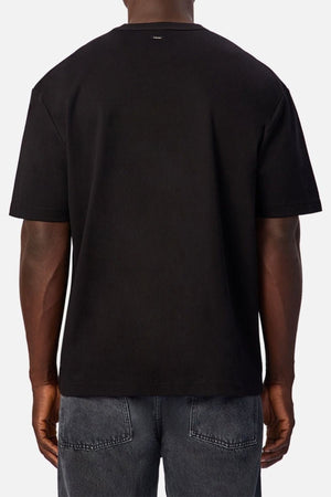 A person is shown from the back against a light gray background, wearing the Industrie Luxe Del Sur Teeโa relaxed-fit top made from 100% cottonโand faded black jeans.