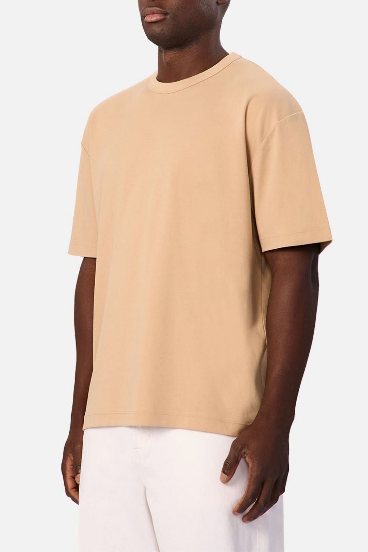 Clad in the Industrie Luxe Del Sur Tee, a relaxed-fit T-shirt made from 100% cotton, and white pants, a person stands against a plain light background.