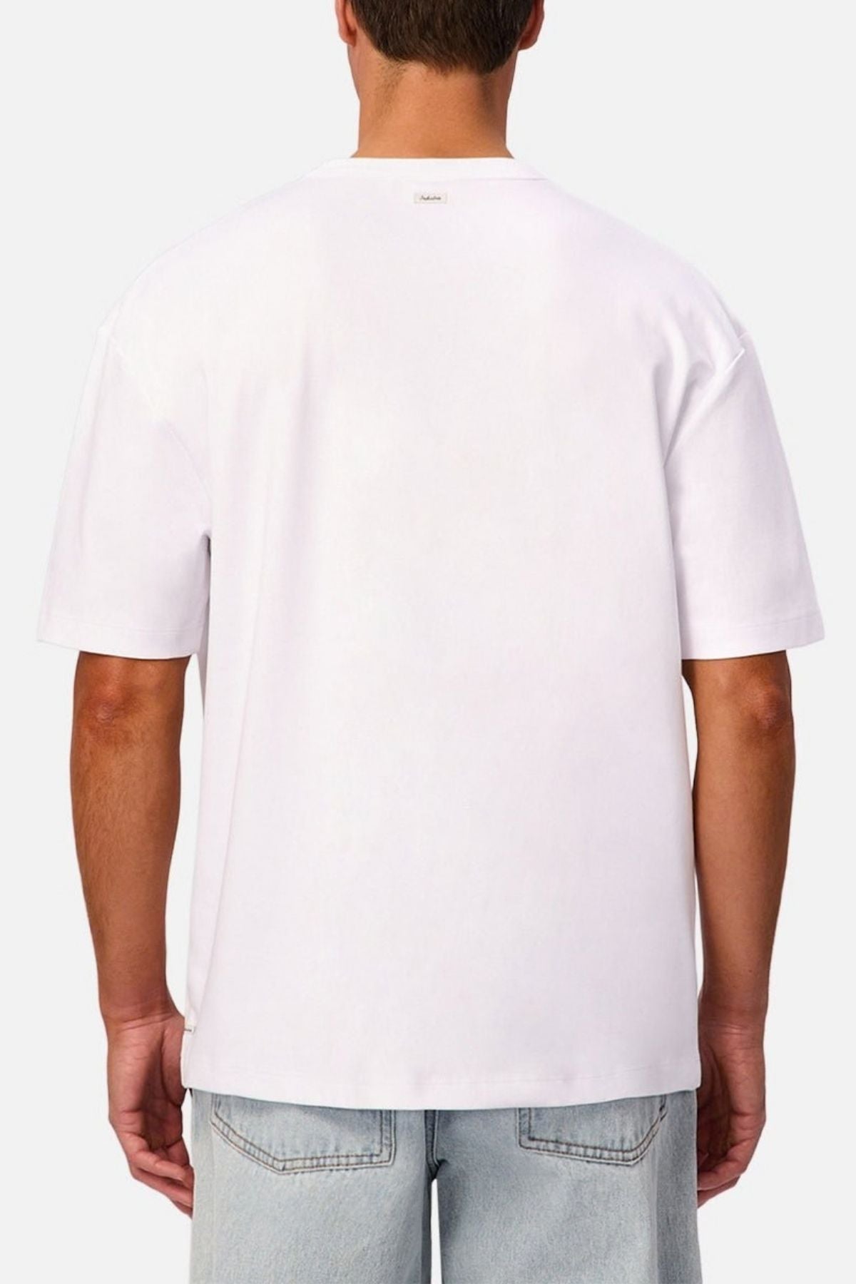 A person is shown from the back against a neutral background, wearing the Industrie Luxe Del Sur Tee—a relaxed-fit, plain white T-shirt made from 100% cotton—paired with light blue jeans.