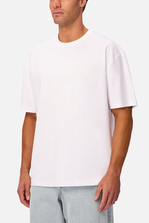 A man wearing the Industrie Luxe Del Sur Tee—a plain, relaxed-fit t-shirt made from 100% cotton—paired with light blue jeans stands against a light gray background.