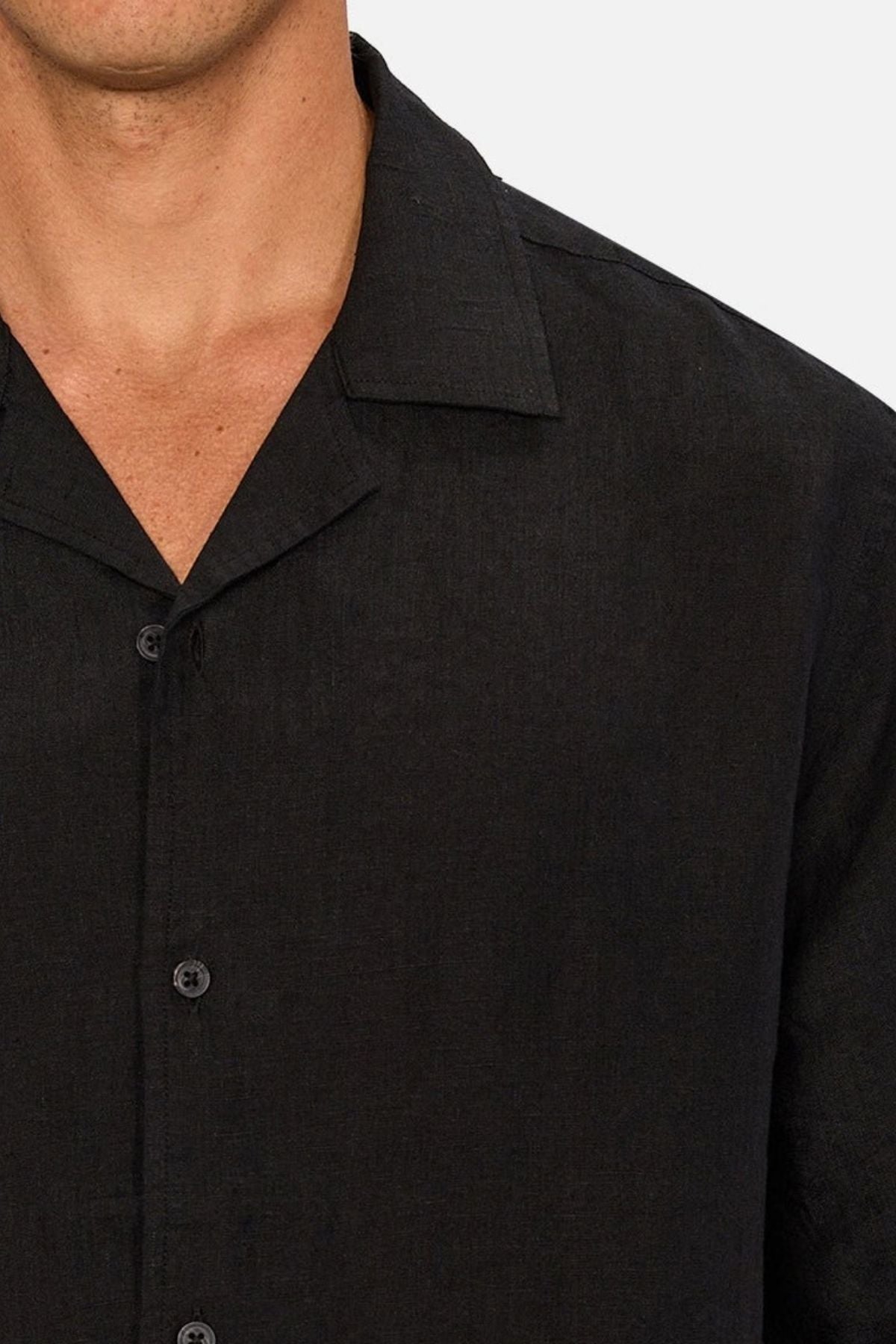 A close-up of a person wearing the Industrie The St Martins Shirt, a black button-up collared linen shirt, shown from the shoulders to mid-chest against a light background.