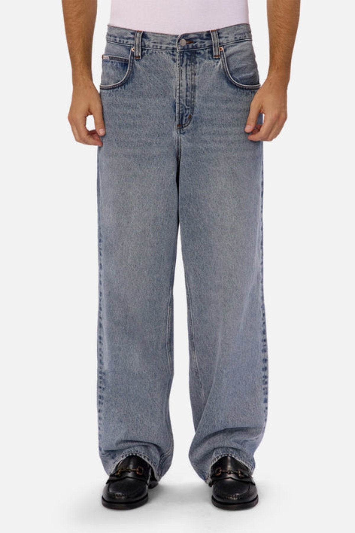 A person wearing Industrie The 80's Jeanโvintage-inspired, loose-fitting wide-leg blue denimโand black loafers stands against a plain white background, with only their lower torso and legs visible.