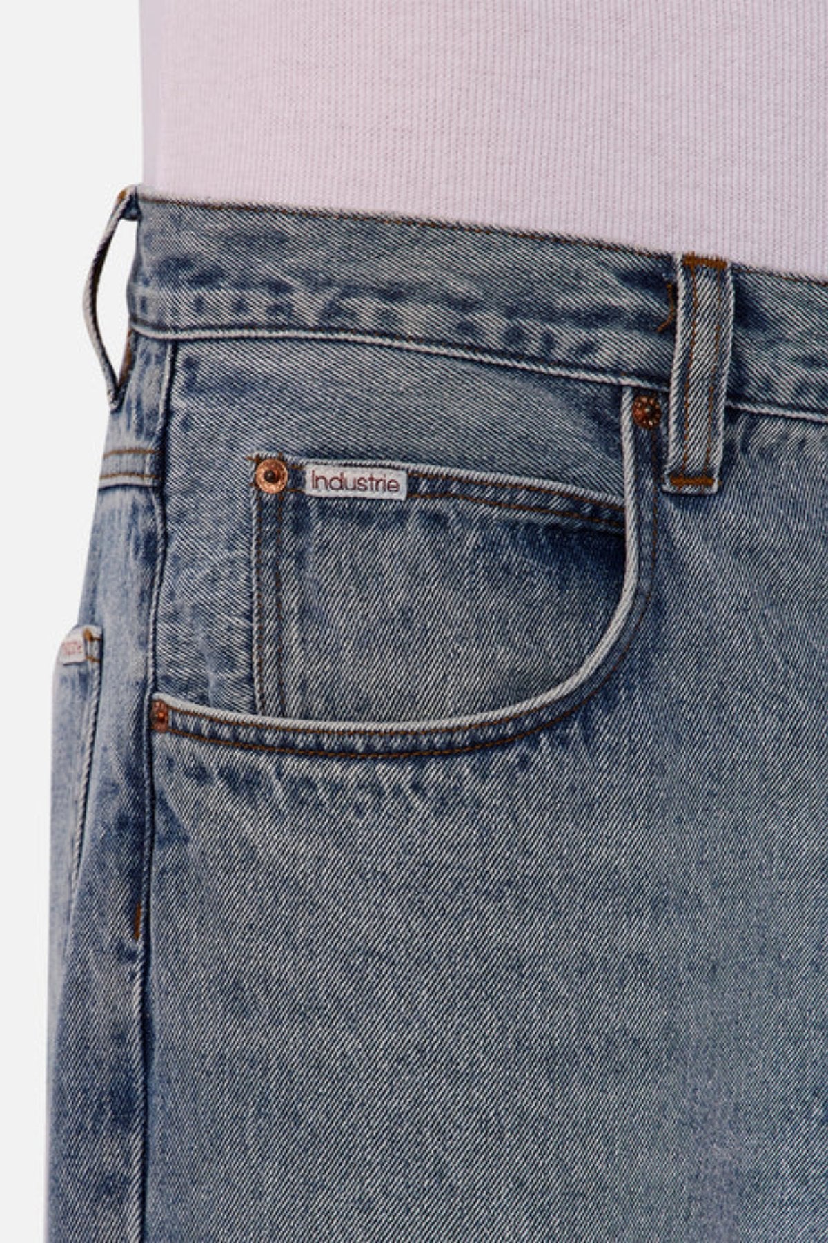 Close-up of Industrie The 80's Jean in light blue vintage-inspired denim, featuring a front pocket with the "Industrie" label, visible stitching, a belt loop, and worn with a tucked-in light shirt.