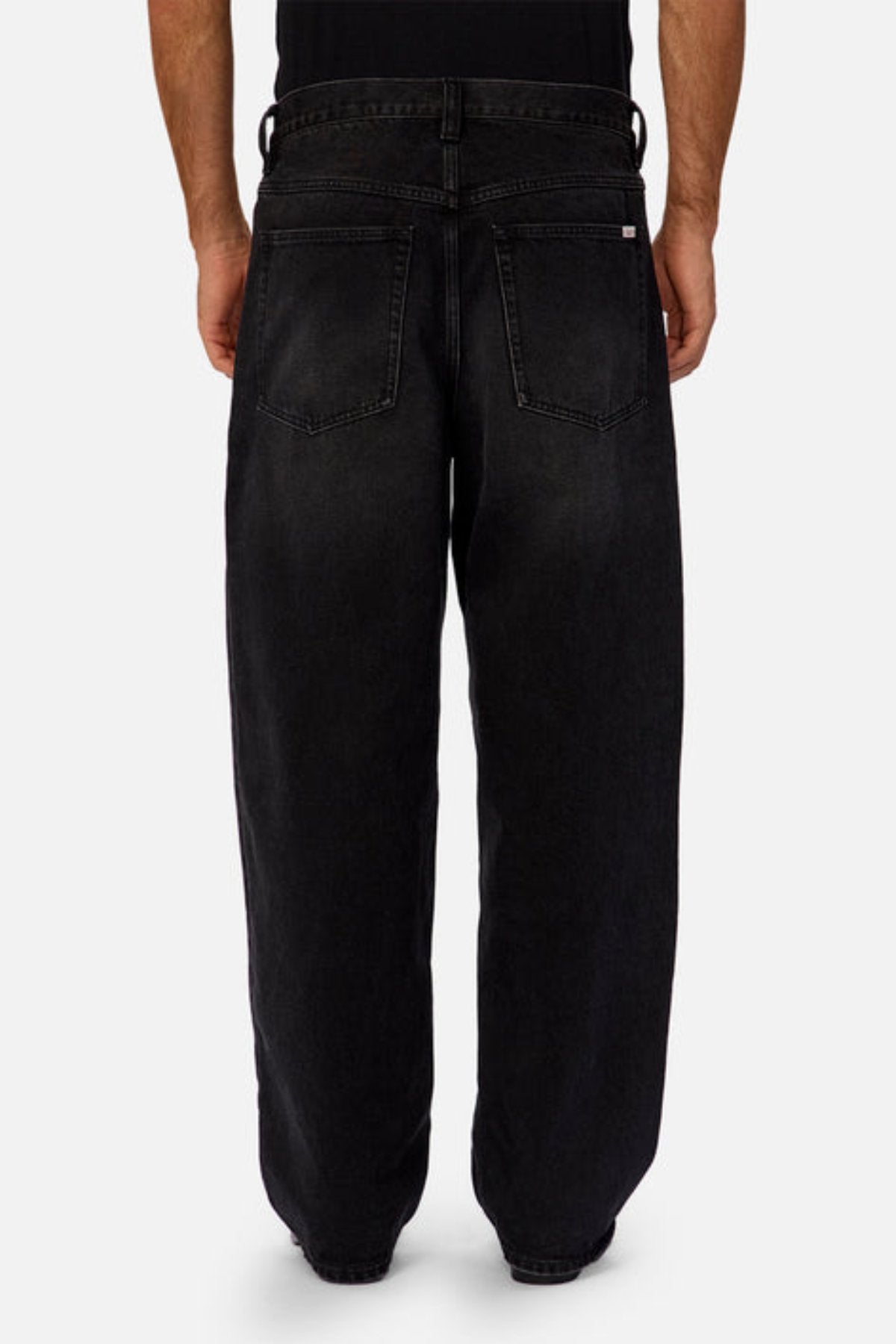A person stands with their back to the camera in Industrie The 80's Jean—loose, vintage-inspired black denim with large back pockets and visible stitching—paired with a black shirt against a plain, light background.