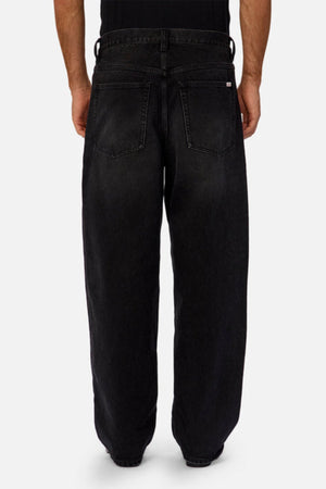 A person stands with their back to the camera in Industrie The 80's Jean—loose, vintage-inspired black denim with large back pockets and visible stitching—paired with a black shirt against a plain, light background.