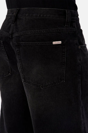 Close-up of the back of a person wearing Industrie The 80's Jean in black denim, featuring a visible back pocket and a small "Industrie" label above it. The person pairs the jeans with a black top.