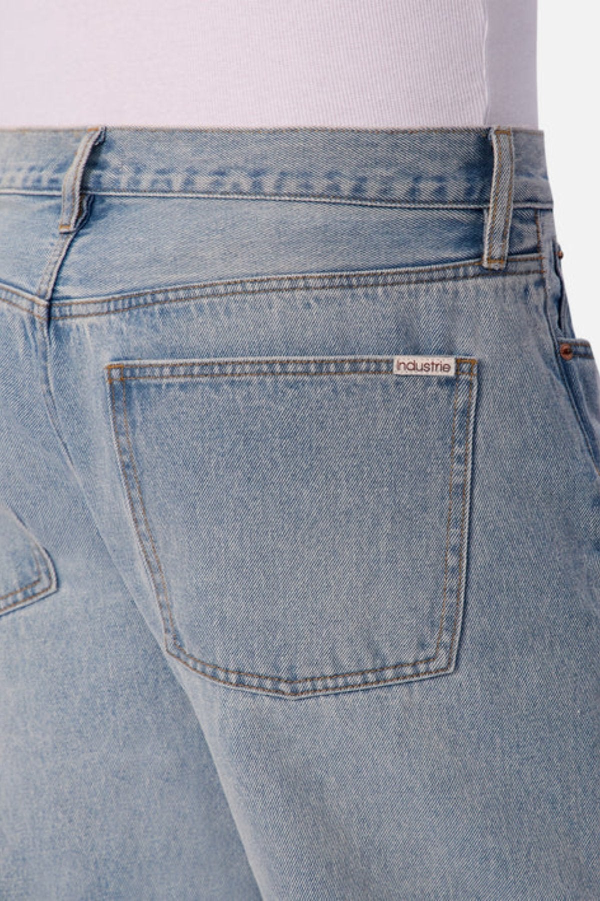 Close-up of the back of a person wearing Industrie The 90's Jean in light blue vintage washed denim and a white top. These jeans have a relaxed straight leg fit and a single back pocket with an "industrie" label above it.