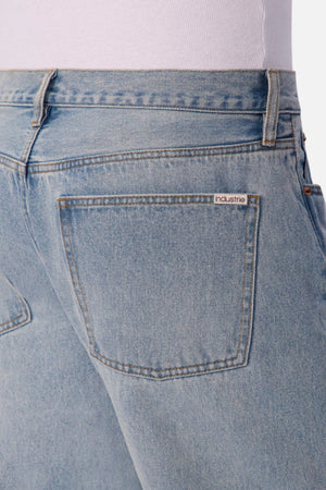 Close-up of the back of a person wearing Industrie The 90's Jean in light blue vintage washed denim and a white top. These jeans have a relaxed straight leg fit and a single back pocket with an "industrie" label above it.