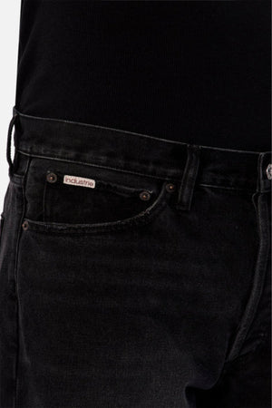 Close-up of a person wearing Industrie The 90's Jean in black vintage washed denim, featuring a relaxed straight leg fit and visible "Industrie" logo on the small pocket, paired with a black ribbed top. Only waist, pockets, and part of thigh are shown.
