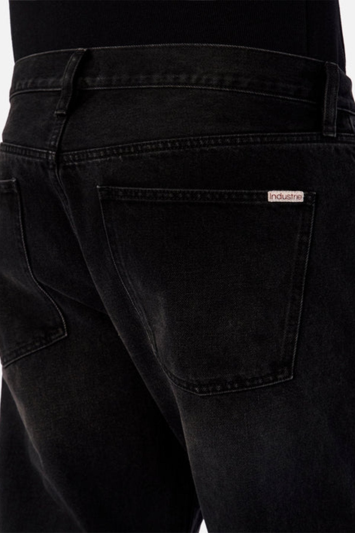 Close-up of the back of a person wearing Industrie The 90's Jean in black vintage washed denim, featuring a visible “Industrie” label above the right pocket. The relaxed straight leg is styled with a black top for a classic look.