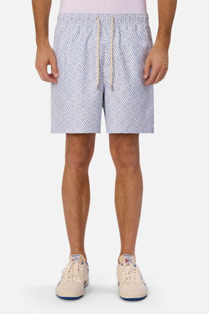 Someone is standing against a plain white background wearing Industrie The Alvarado Swim Shorts and white sneakers. The swim shorts, celebrated for their intricate geometric design and regular tailored fit, pair well with the sneakers featuring blue accents. The person's upper body is not visible.