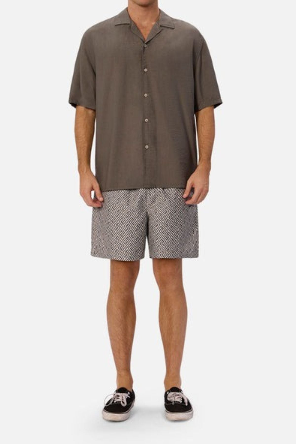 A person wearing a short-sleeved, olive-green shirt and Industrie The Alvarado Swim Short stands against a plain white background. The quick-drying shorts feature a black-and-white pattern, perfectly complemented by their black sneakers with white laces suited for aquatic leisure.