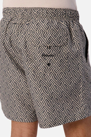 A close-up of someone wearing the Industrie The Alvarado Swim Short, showcasing its geometric pattern in black and gray. Ideal for water activities, these quick-drying shorts come with an elastic waistband, a back pocket secured by a small button, and proudly display the brand's logo.