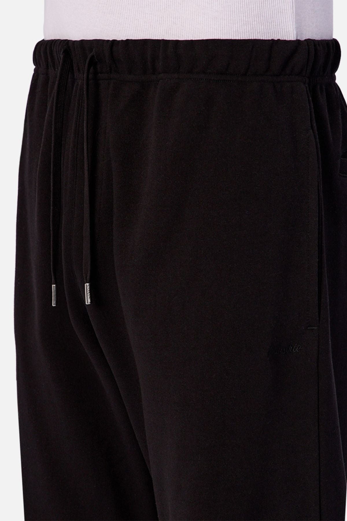 A close-up of a person wearing the Industrie The Astoria Lux Tech Trackpant with a drawstring waistband and side pockets, paired with a white shirt. These sweatpants feature metal-tipped drawstrings and provide premium comfort for casual style.