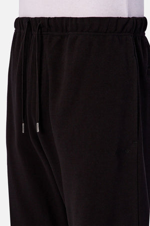 A close-up of a person wearing the Industrie The Astoria Lux Tech Trackpant with a drawstring waistband and side pockets, paired with a white shirt. These sweatpants feature metal-tipped drawstrings and provide premium comfort for casual style.