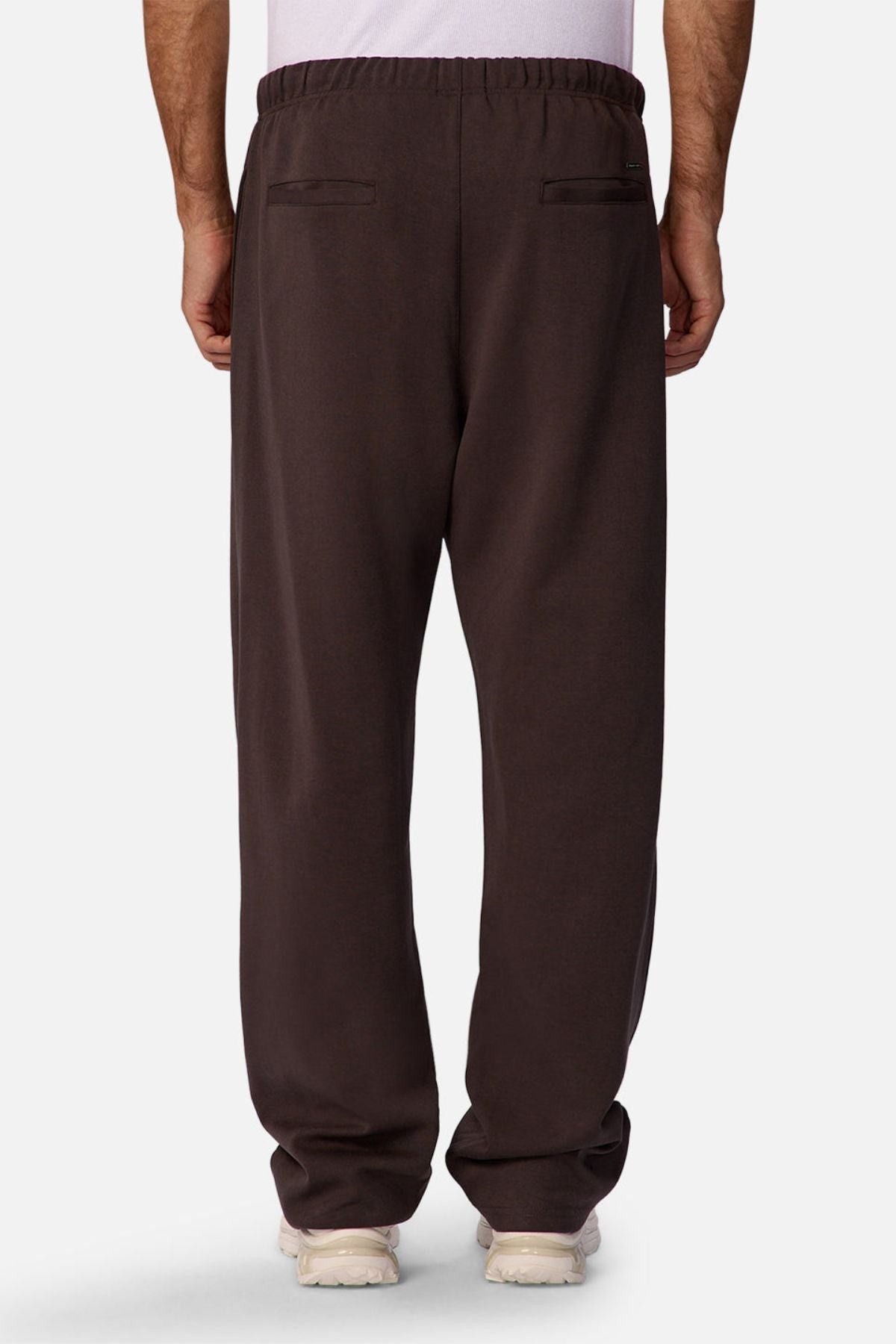 Someone wearing the Industrie The Astoria Lux Tech Trackpant in dark brown, featuring an elastic waistband and two back pockets, is shown from the back against a plain light background for a casual style look.