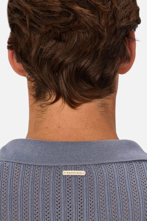 A person with short, wavy brown hair is seen from behind, wearing the Industrie The Bellano Polo in light blue, crafted from 100% cotton with a textured knit and a small "INDUSTRIE" label on the back collar.