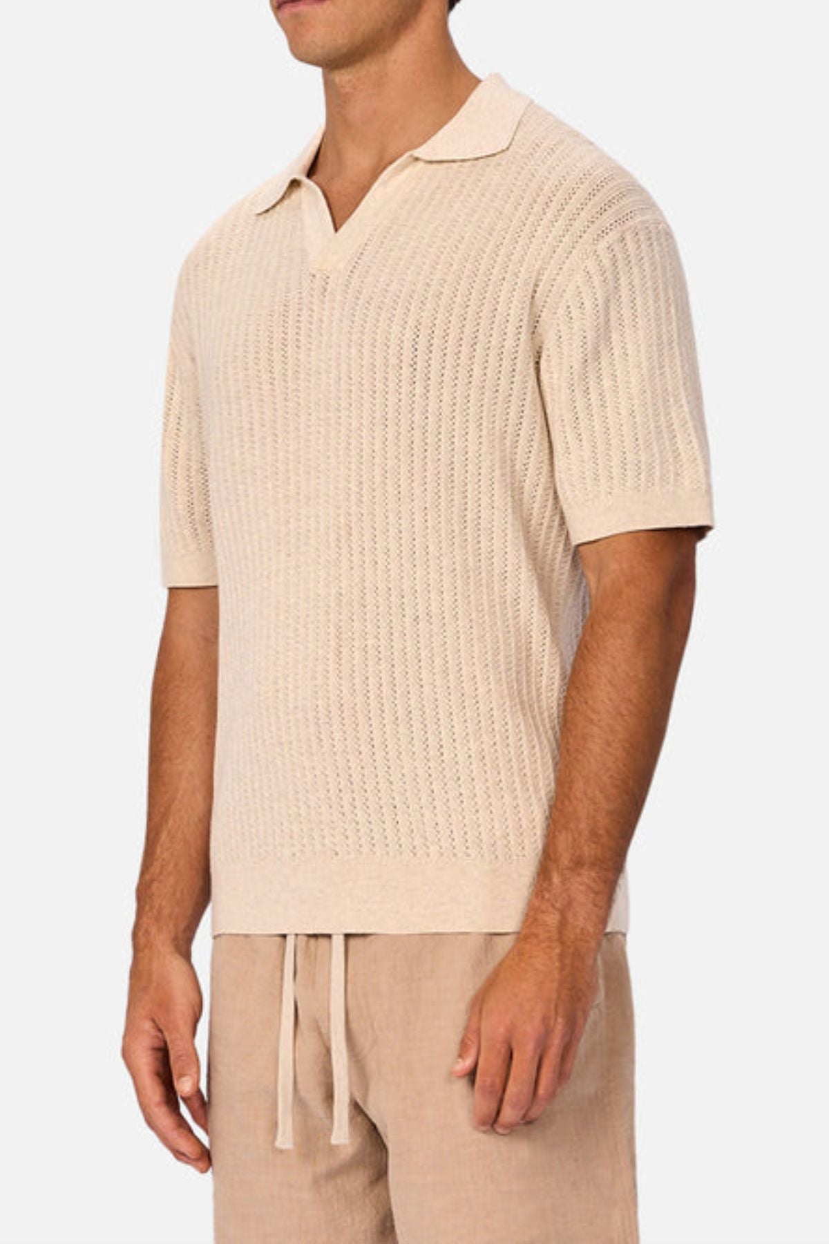 A man wears the Industrie The Bellano Polo, a light beige breathable cotton shirt, with matching drawstring linen shorts, standing against a plain white background.
