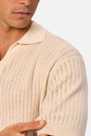 A man, shown from the shoulders up, holds the sleeve of his beige Industrie The Bellano Polo to display its textured, ribbed cotton fabric and breathable design.