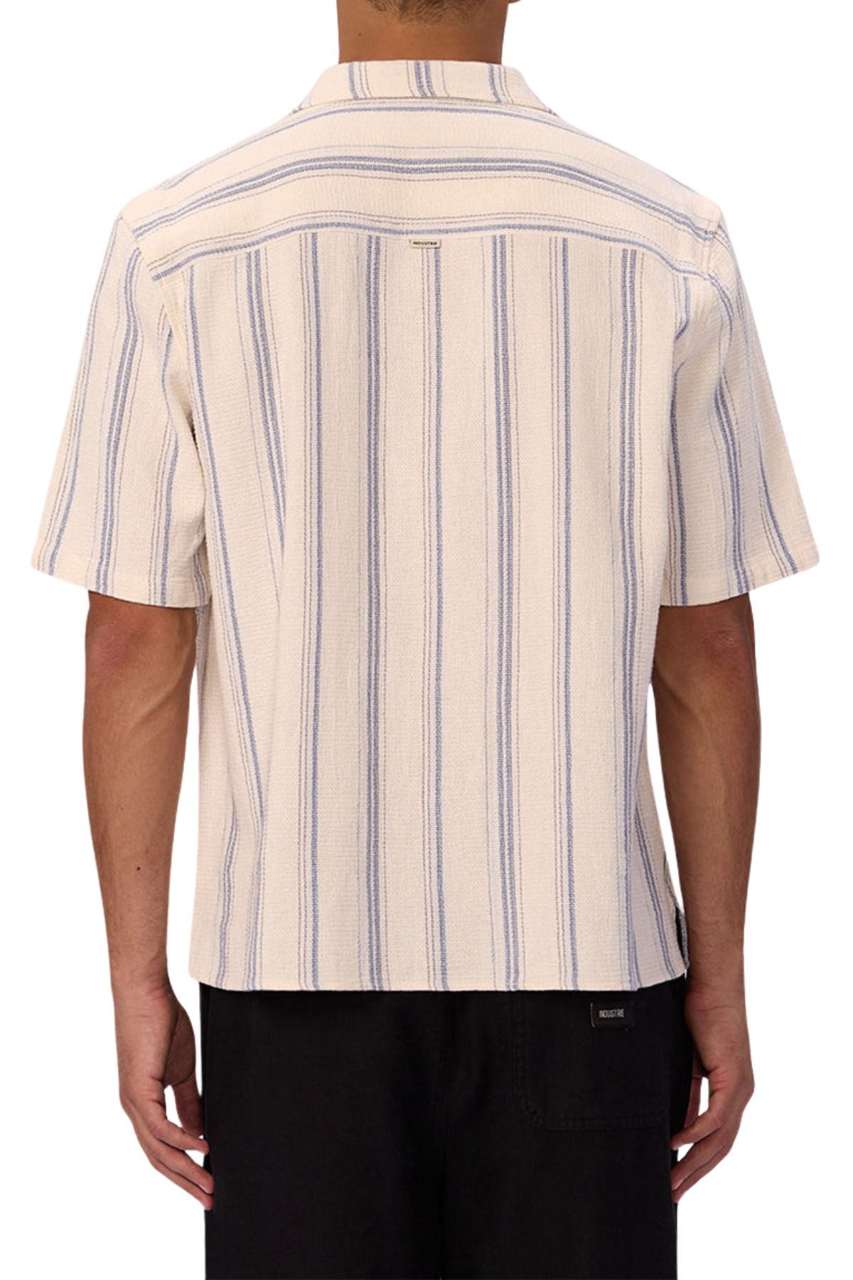 A person is seen from behind wearing the Industrie The Bowment Short Sleeve Shirt in cream with vertical blue textured stripes, paired with black pants—a stylish, casual wardrobe choice.