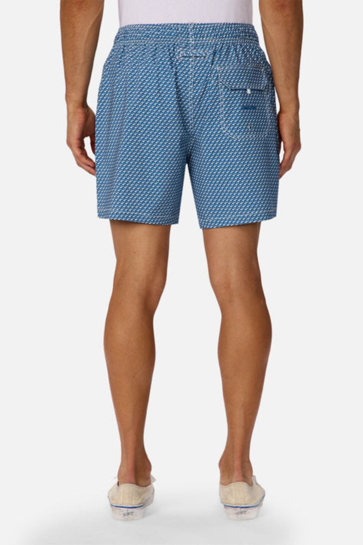A person faces away from the camera, wearing Industrie The Cayman Swim Short with an abstract print, paired with a white shirt and light slip-on shoes against a plain white background.