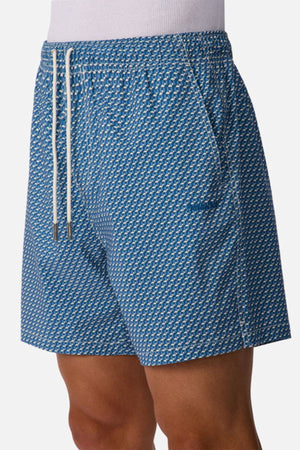A person wears Industrie The Cayman Swim Short, featuring a subtle geometric abstract pattern, white drawstrings, and practical side pockets, standing against a plain white background.