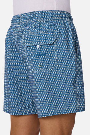 A person wearing Industrie The Cayman Swim Short, featuring a blue and white abstract pattern, back pocket, and white stitching, shown from the waist down and viewed from behind.