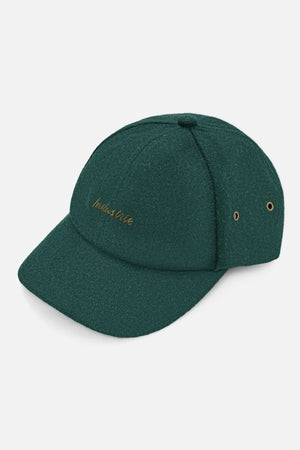 The Industrie The Claude Cap is a dark green wool blend cap with "indaba tribe" embroidered in gold on the front, two metal eyelets on the side, a curved brim, and an adjustable strap for a perfect fit.