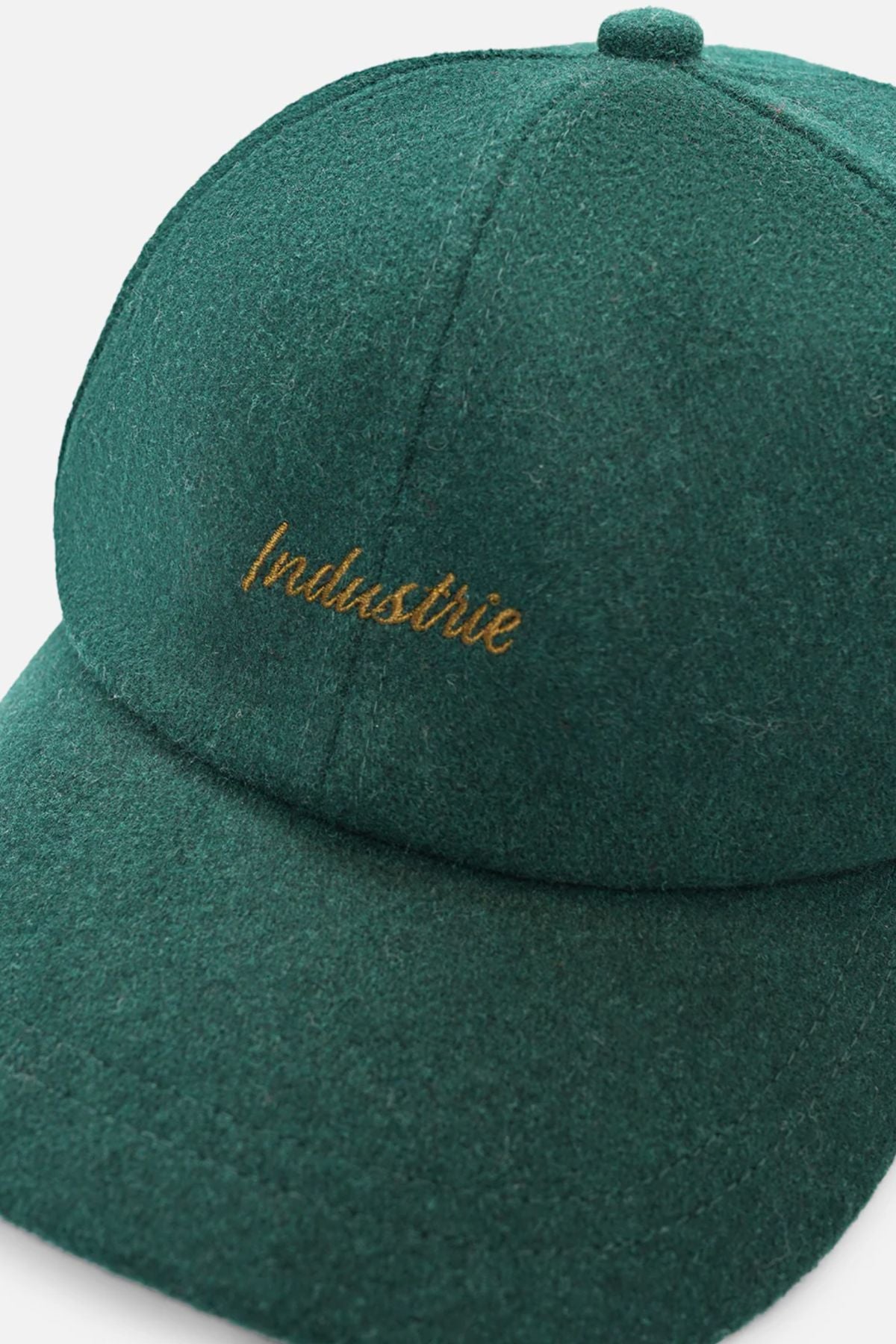 A close-up of the Industrie The Claude Cap, a dark green wool blend cap featuring gold "Industrie" embroidery on the front and an adjustable strap.