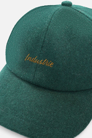 A close-up of the Industrie The Claude Cap, a dark green wool blend cap featuring gold "Industrie" embroidery on the front and an adjustable strap.