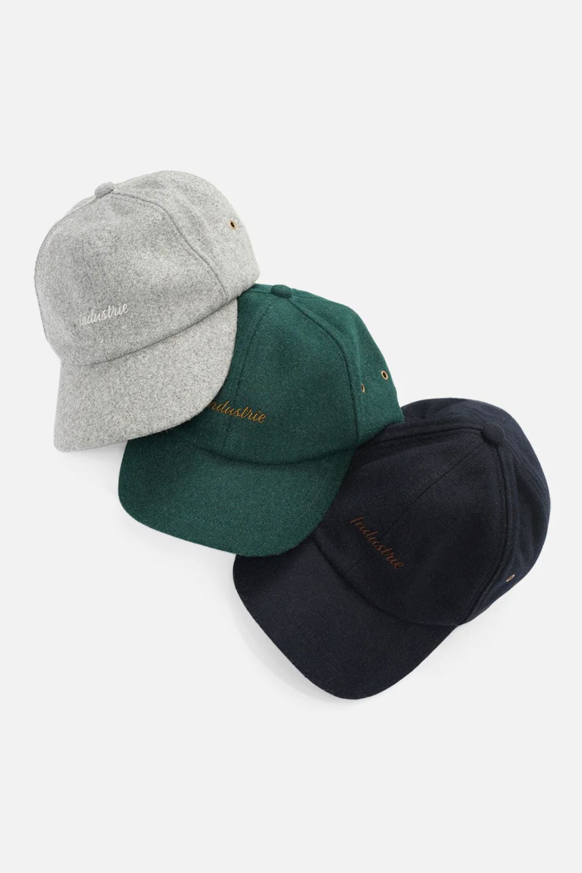 Three Industrie The Claude Caps in grey, dark green, and black overlap on a white background. Each wool blend cap features small front-left embroidered text and an adjustable strap for comfort.