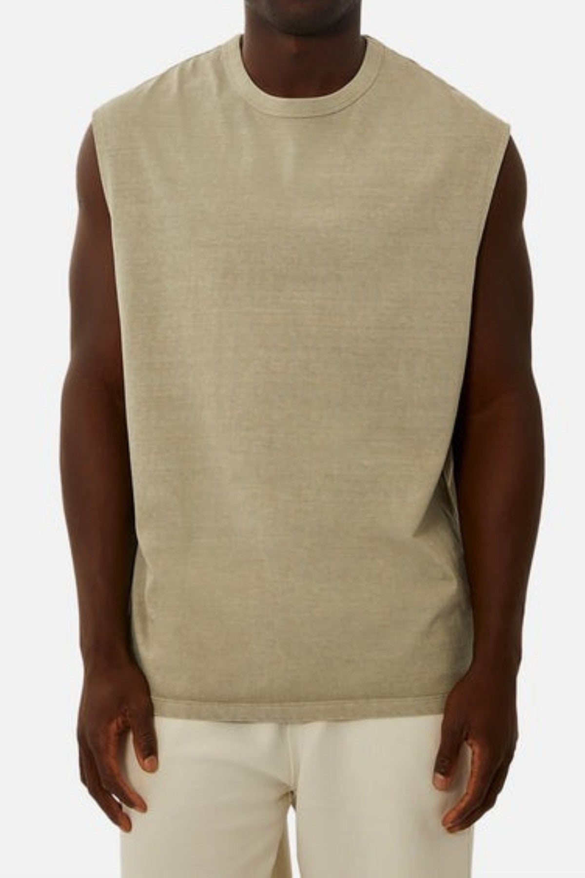A person wearing the Industrie The Del Sur Sleeveless Tee, crafted from 100% cotton in a beige hue, stands against a plain background facing the camera. Their relaxed arms rest at their sides, enhancing the effortlessly chic appearance of their white pants and oversized fit.