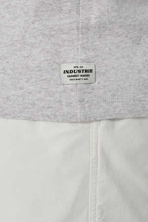 A close-up of the Industrie The Del Sur Sleeveless Tee in light grey cotton, featuring a small white "INDUSTRIE GARMENT MAKERS" label above white pants. The stitching, texture, and oversized fit are clearly shown.