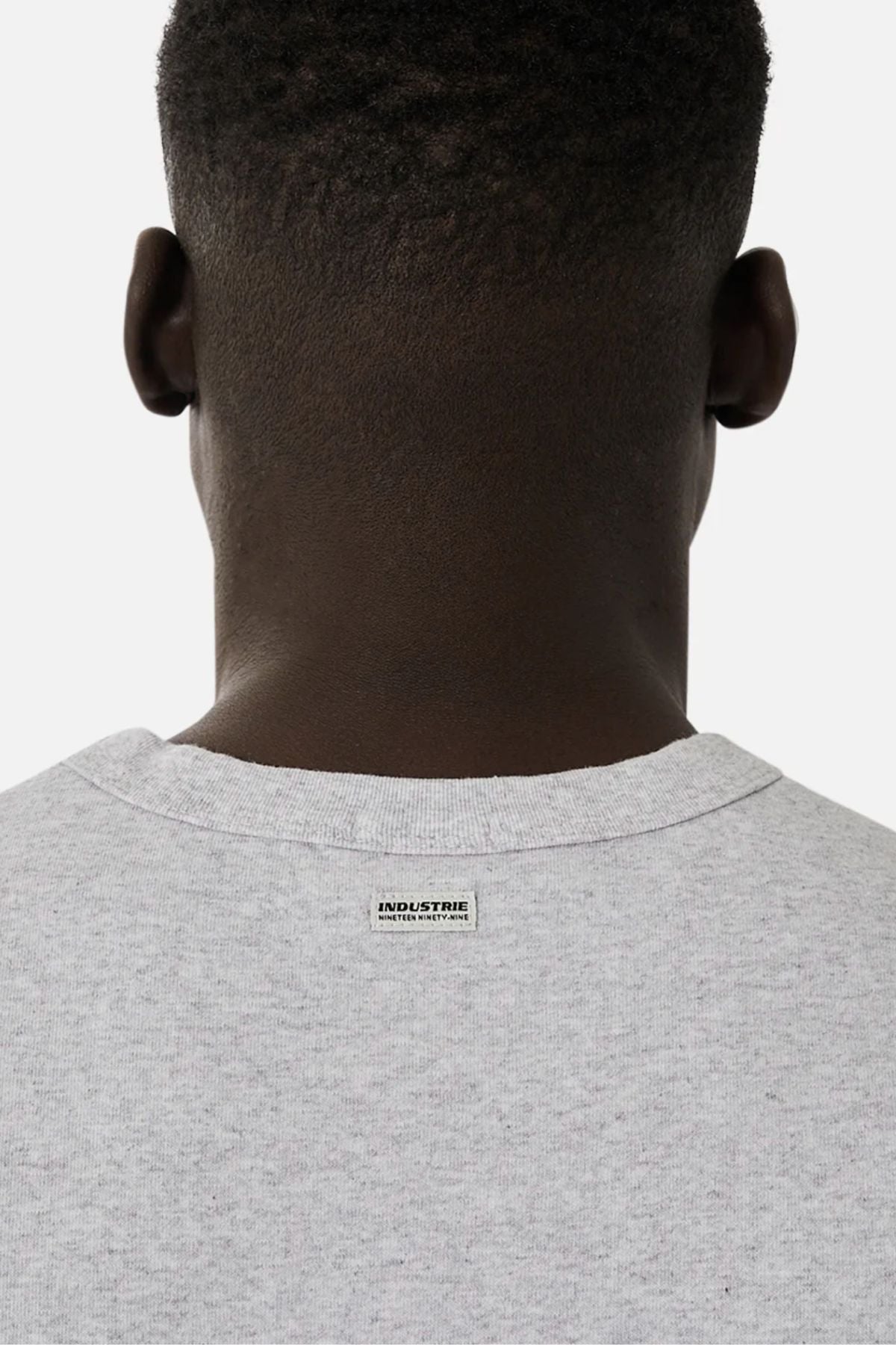 The back view shows a person wearing the Industrie The Del Sur Sleeveless Tee in light gray cotton, featuring a small "INDUSTRIE" tag at the neckline. The background is plain white.