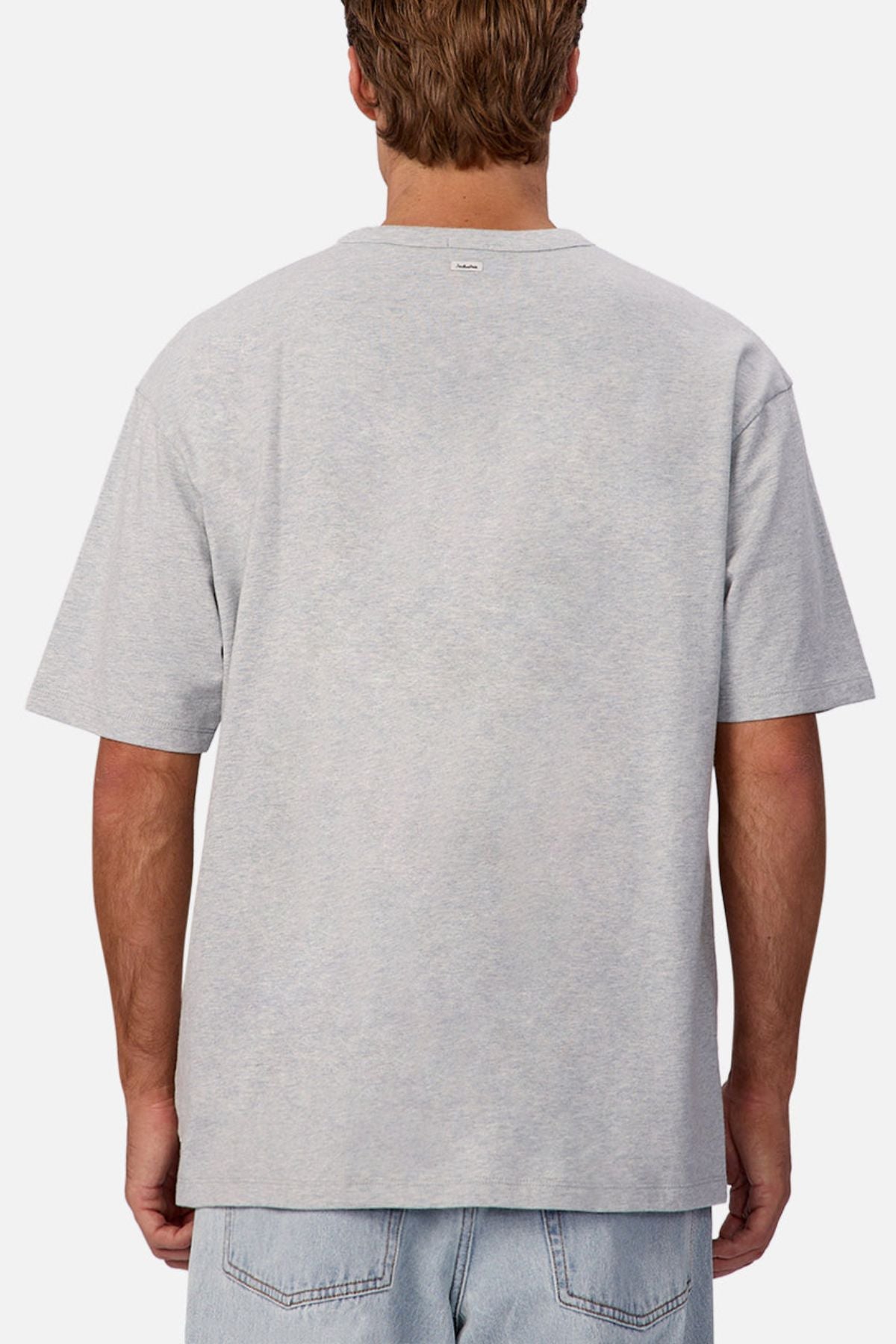 A person with short brown hair is shown from the back, wearing an Industrie The Del Sur Tee in light gray heavyweight fabric with an oversized fit and light blue denim jeans against a plain white background.