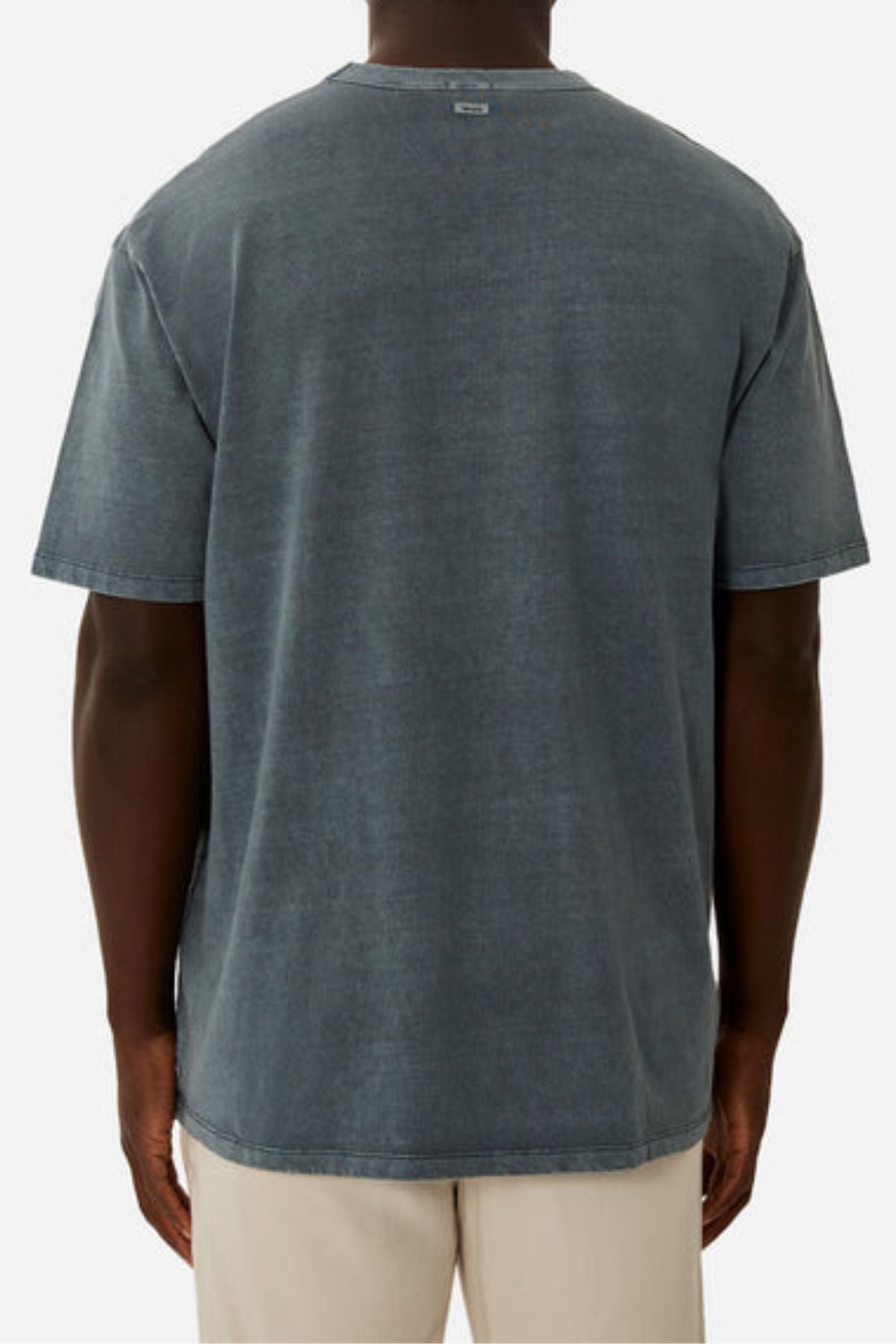 A person wearing an oversized Industrie The Del Sur Tee in heavyweight faded dark gray, paired with light beige pants, shown from the back against a plain light background.