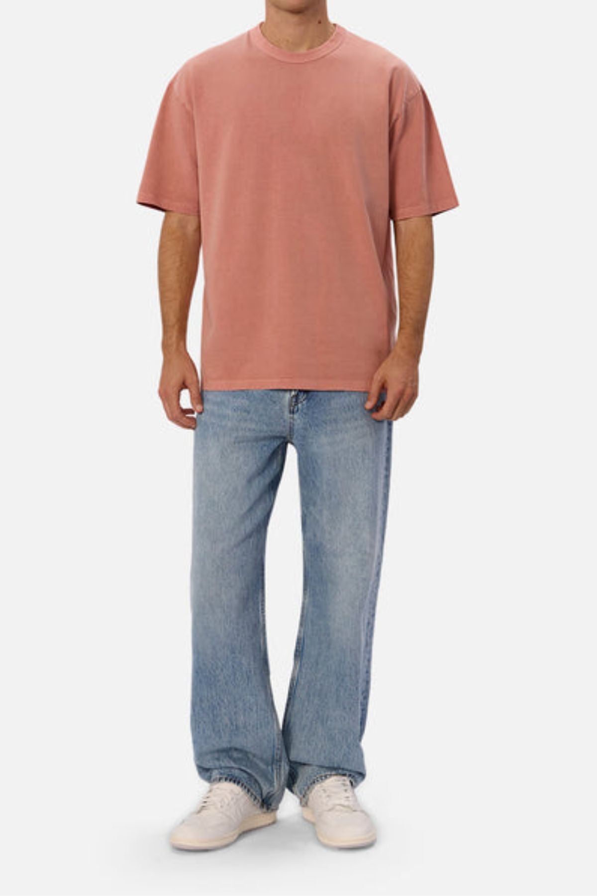 Wearing Industrie's The Del Sur Tee in a loose-fitting pink style, an individual pairs it with light blue wide-leg jeans and white sneakers while standing against a plain white background. Made from heavyweight fabric, the outfit conveys a casual and relaxed vibe.