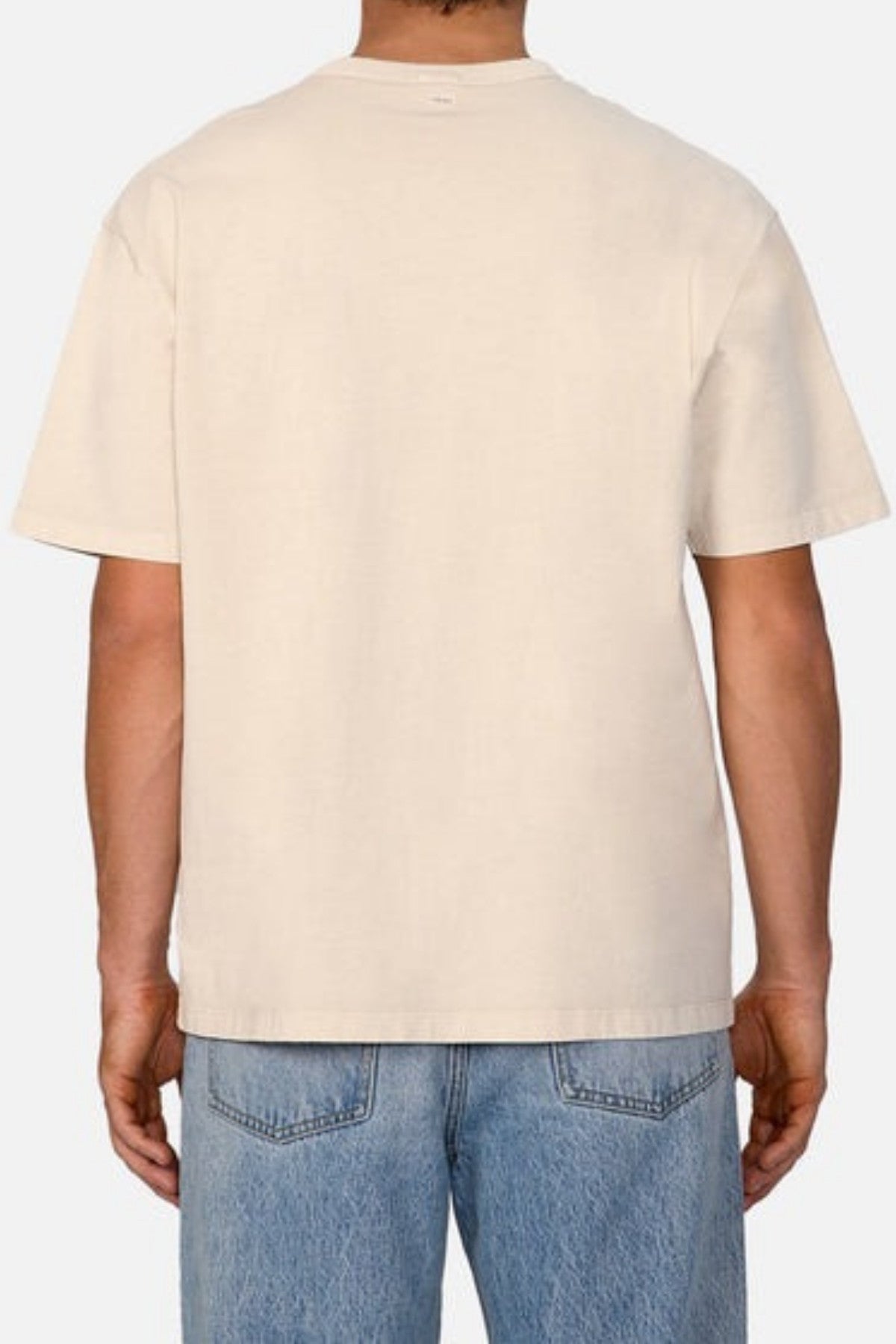 Against a neutral background, an individual is seen from behind showcasing the Industrie logo, while wearing the Industrie The Del Sur Tee in an oversized fit paired with light blue jeans.