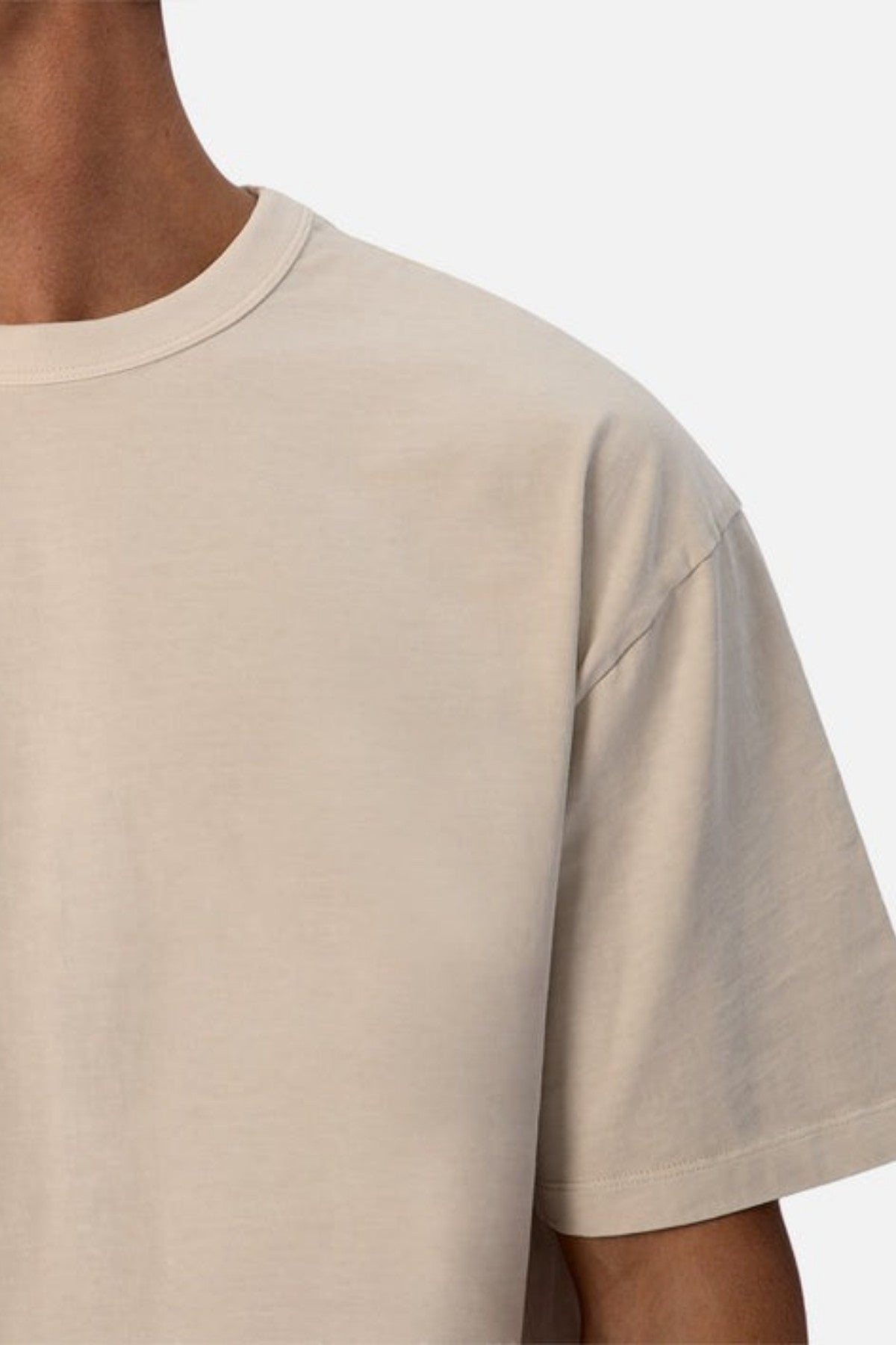 A close-up of a person wearing the Industrie The Del Sur Tee, which features an oversized fit in a plain beige color. The image showcases the shoulder and part of the upper chest, emphasizing its simple and casual style made from heavyweight fabric against a light gray background.