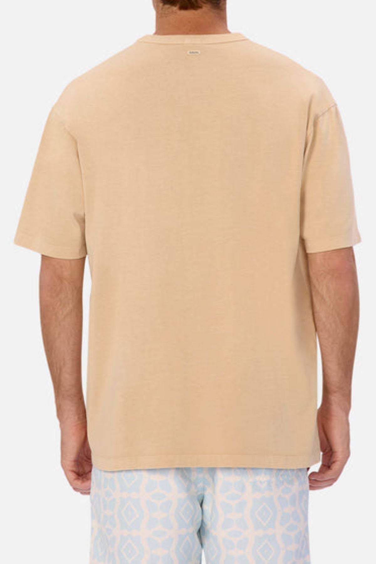 Rear view of a person wearing an oversized Industrie The Del Sur Tee in heavyweight fabric paired with light blue patterned shorts. The background is plain white.