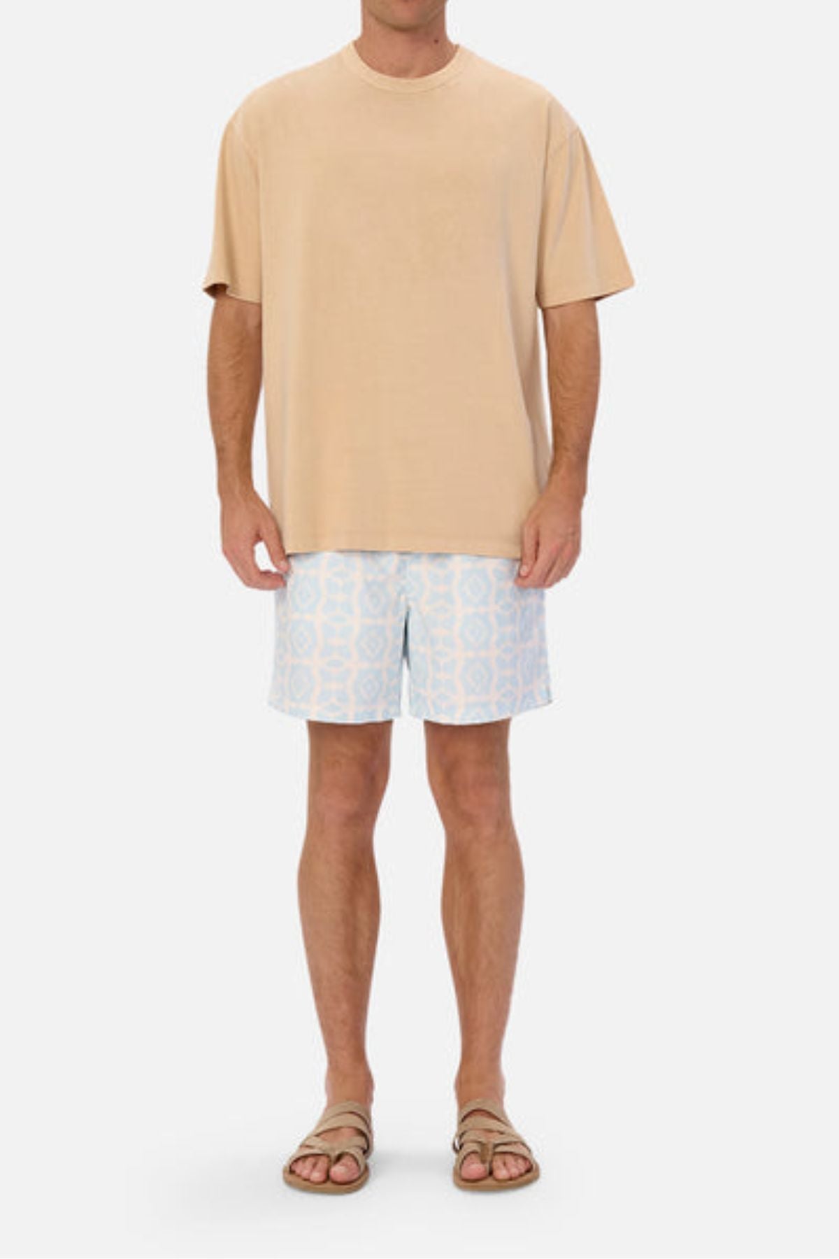 A person wearing an oversized fit beige Industrie The Del Sur Tee, light blue and white patterned shorts, and brown sandals stands against a plain white background. The heavyweight fabric of the tee adds a touch of casual elegance to their laid-back ensemble.