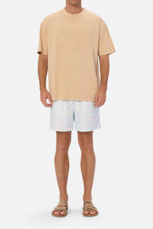 A person wearing an oversized fit beige Industrie The Del Sur Tee, light blue and white patterned shorts, and brown sandals stands against a plain white background. The heavyweight fabric of the tee adds a touch of casual elegance to their laid-back ensemble.