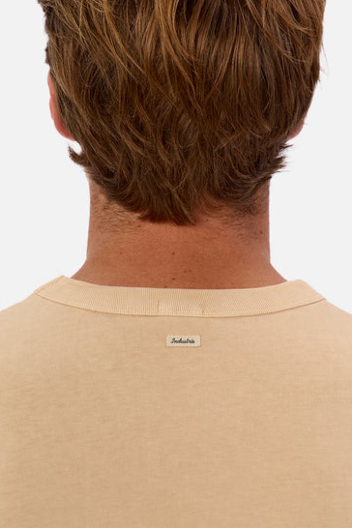 View from behind of a person with light brown hair wearing an oversized Industrie The Del Sur Tee crafted from heavyweight fabric. A small label is visible on the back of the shirt, set against a plain white background.