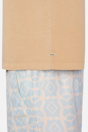 A close-up of the Industrie The Del Sur Tee in heavyweight fabric, paired with light blue patterned pants, showcases a harmonious blend of fashion elements. The geometric design and small logo on the pants perfectly complement the tee's label, creating a stylish contrast against the plain background. Both pieces feature an oversized fit for effortless style.