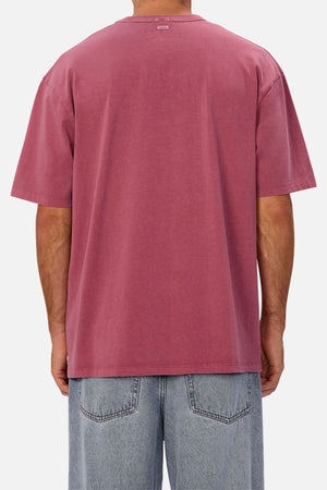 A person shown from the back against a plain white background wears an oversized Industrie The Del Sur Tee in faded rose and light blue denim jeans, with the T-shirt made from heavyweight fabric.