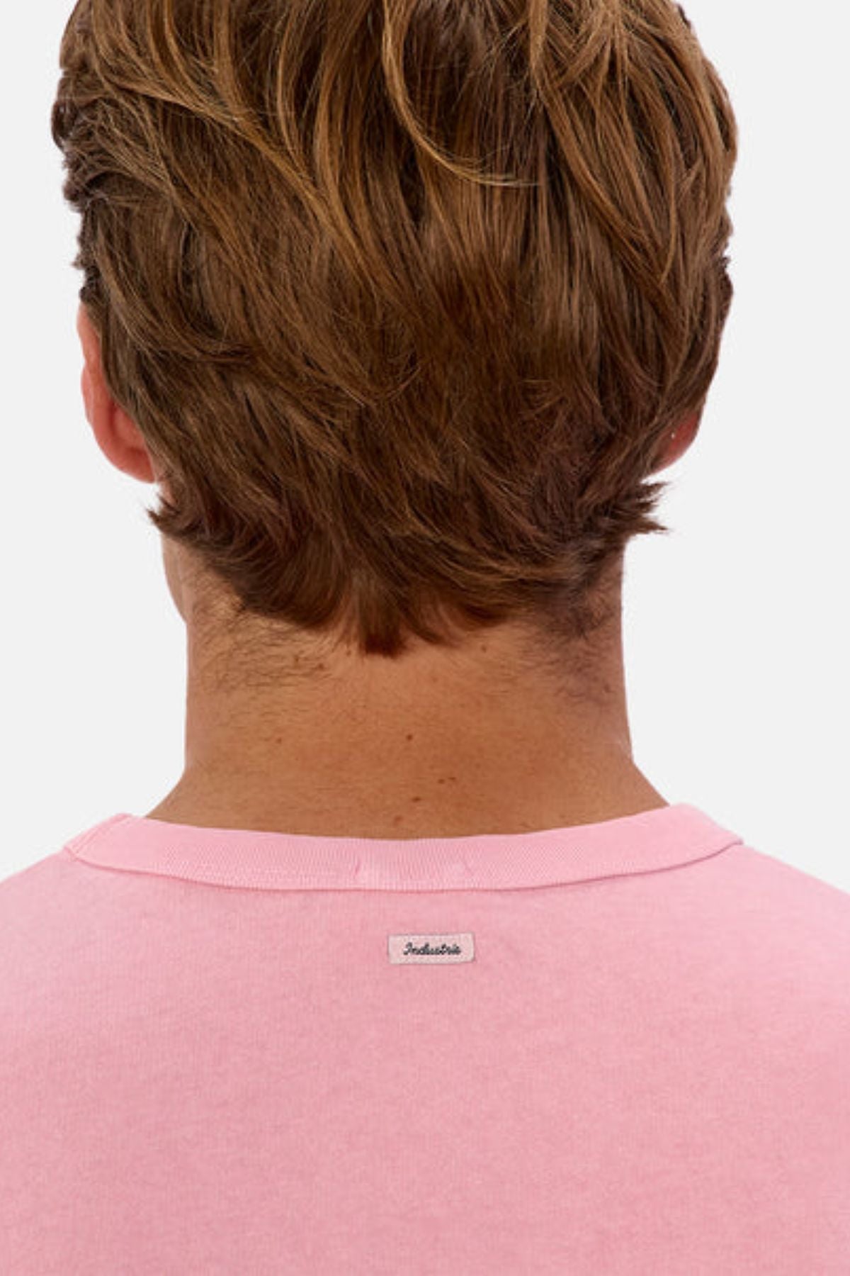 Rear view of a person with light brown hair wearing an oversized pink sweater labeled "Industrie The Del Sur Tee" on the back, crafted in heavyweight fabric. The background is plain white.