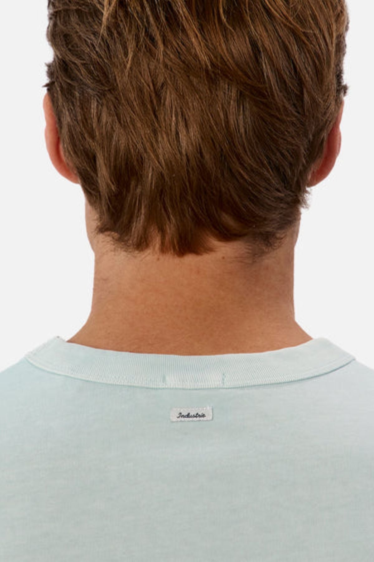 Rear view of a person with short brown hair wearing the "Industrie The Del Sur Tee," crafted from heavyweight fabric. The label "Industrie" is visible on the back of the light blue, oversized fit shirt against a plain white background.